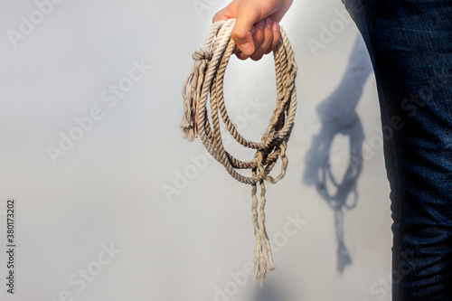 Close up shot of male holding a lasso or cowboy rope in his hands against a white wall.