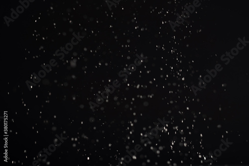 Snow background. White bokeh lights isolated on black. Winter night. Dark blizzard sky. Defocused ice flakes texture Christmas decorative abstract wallpaper.