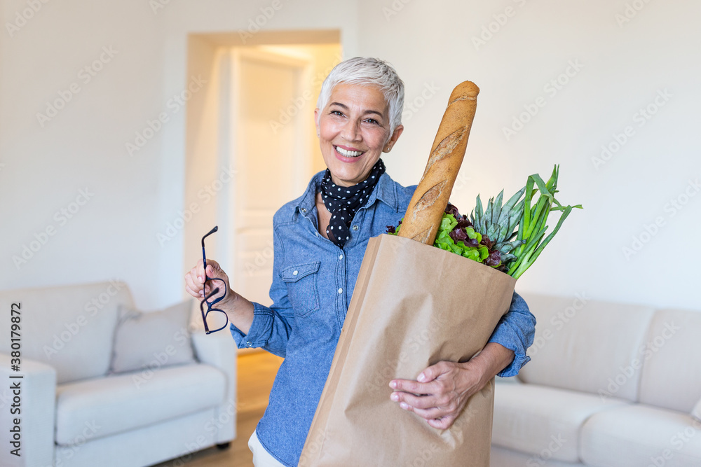Healthy positive happy woman holding a paper shopping bag full of fruit and vegetables. Portrait of beautiful senior woman grocery shopping bag with vegetables at home Healthy positive happy woman holding a paper shopping bag full of fruit and vegetables. Portrait of beautiful senior woman grocery shopping bag with vegetables at home