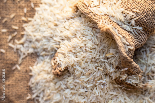 Close up shot of Raw Basmati white rice in a gunny bag on brown surface.