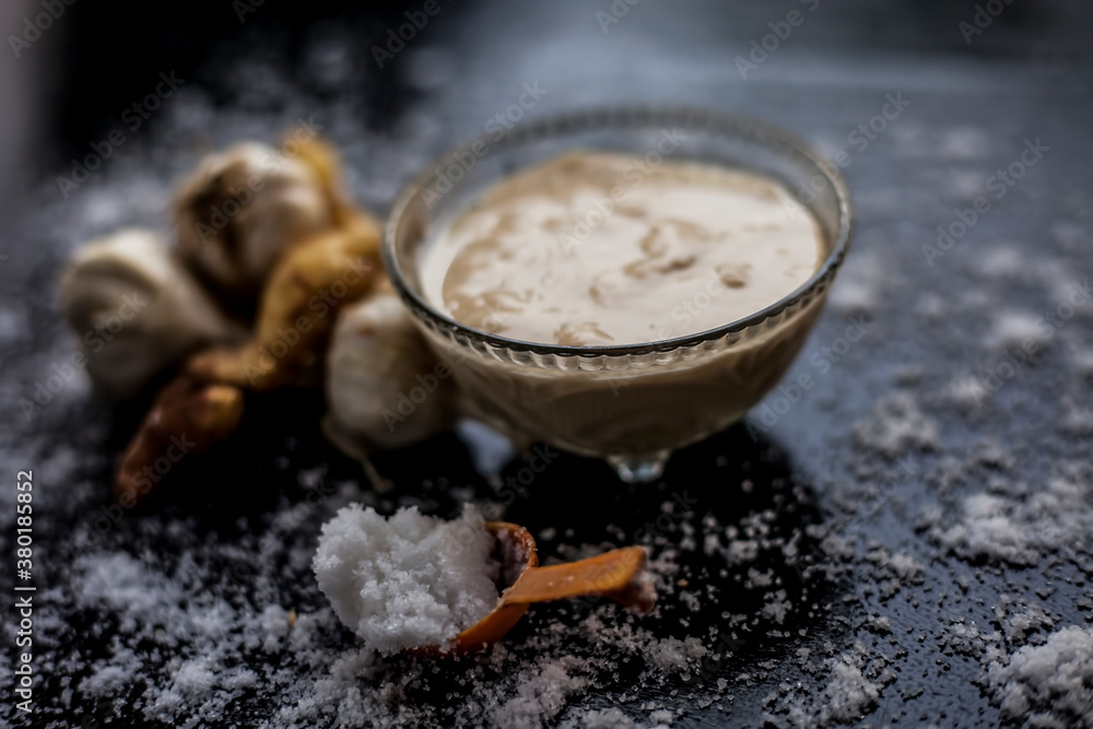 Shot of freshly ground garlic and ginger paste in a glass bowl on a black surface along with raw ginger, and some garlic with salt on sprinkle on the surface. Shot of freshly ground garlic and ginger paste in a glass bowl on a black surface along with raw ginger, and some garlic with salt on sprinkle on the surface.