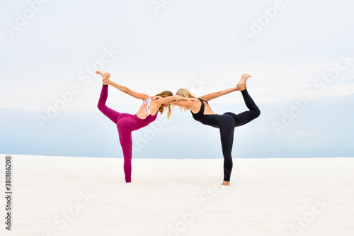 Two beautiful young women performing yoga pose nataradzhasana together on the beach photo