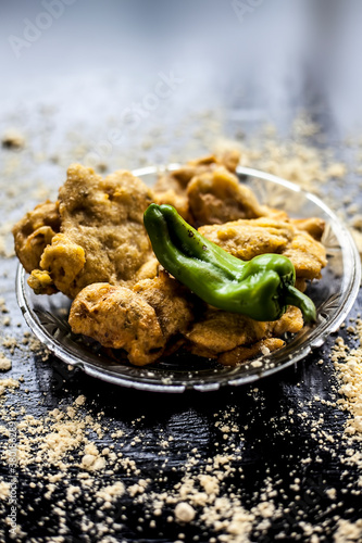 Famous Aloo pakora/ aloo bhajia in a glass plate with green chili and some chickpea flour spread on a surface.Shot of alu bhajiya on a transparent glass plate. Vertical shot. photo