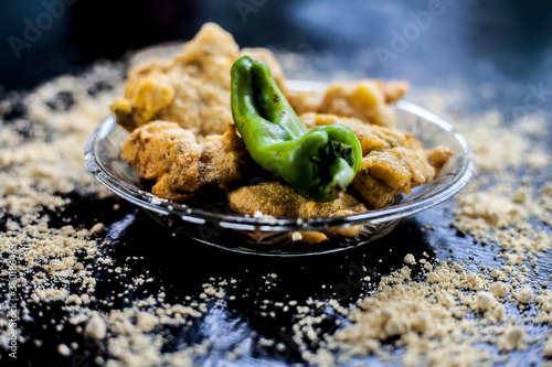 Famous Aloo pakora/ aloo bhajia in a glass plate with green chili and some chickpea flour spread on a surface.Shot of alu bhajiya on a transparent glass plate. Horizontal shot. photo