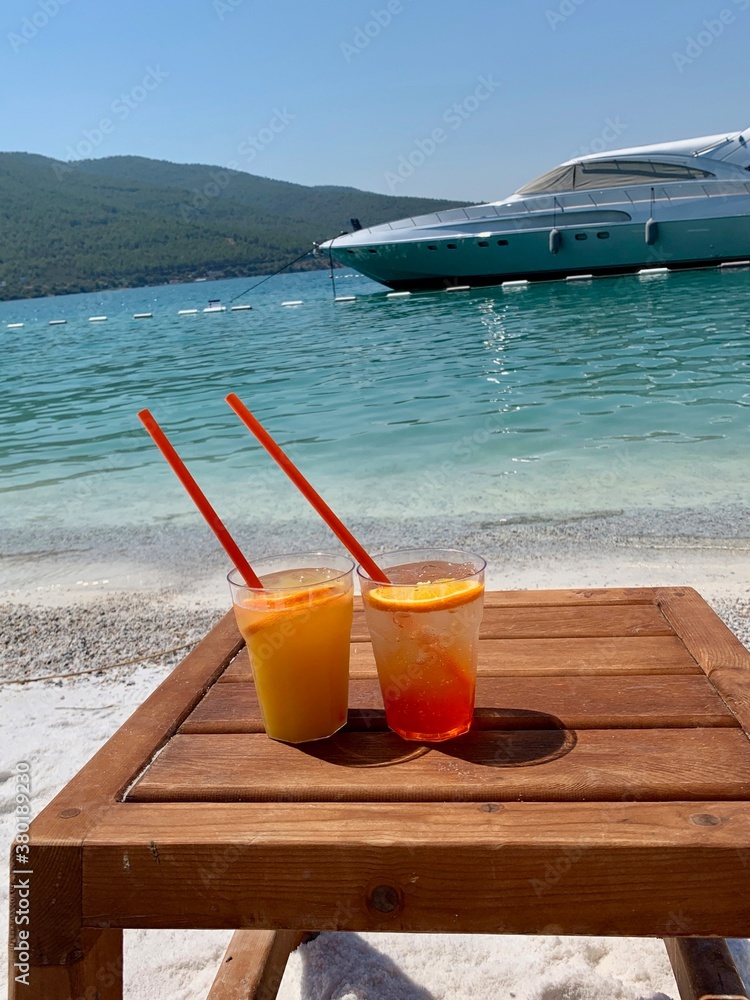 Two glasses of Italian Aperol spritz alcohol cocktail with ice and blood orange slices. Summer refreshing cocktail drink glasses on a wooden tray against the background of the emerald Aegean Sea and a