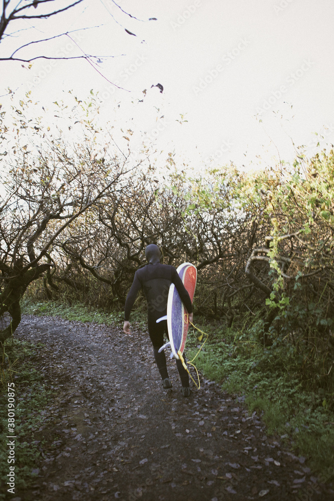 Surfer in wetsuit running on trail with surfboard Surfer in wetsuit running on trail with surfboard