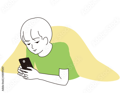 スマートフォンをうつ伏せになって見つめる男の子