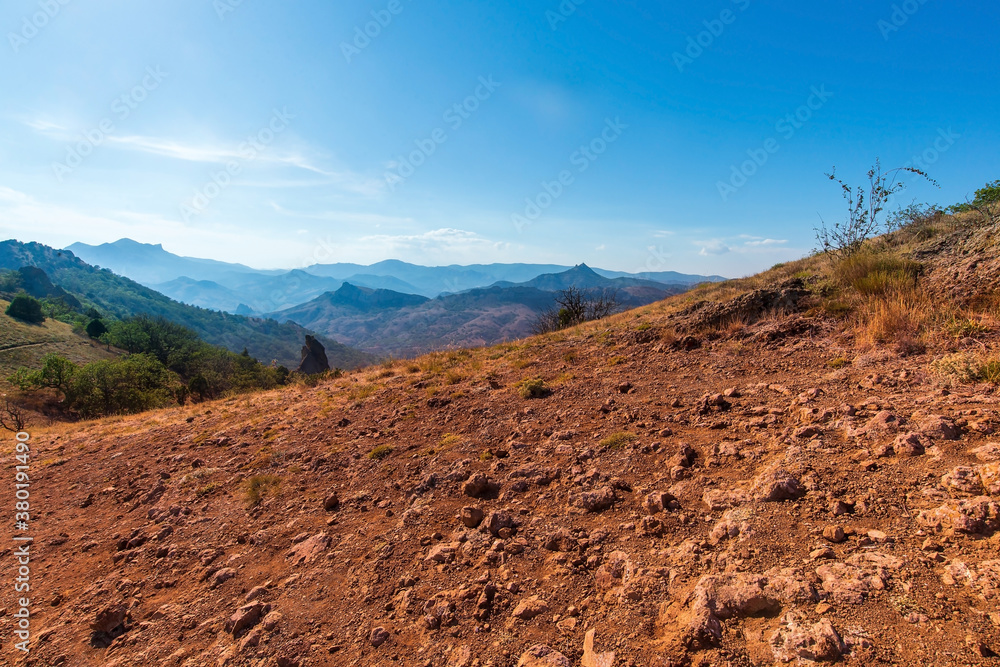 Mountain slope with red earth against the background of mountain peaks, Crimea, Kardag reserve.