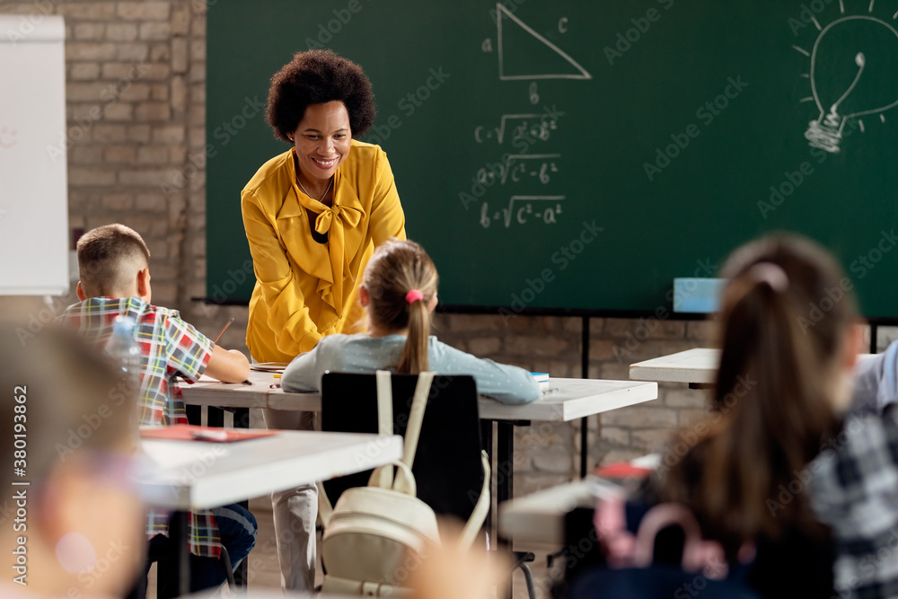 Happy black elementary school teacher taking to her students in the ...