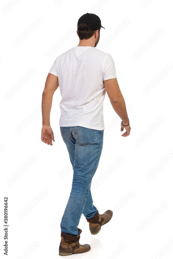 Rear View Of Walking Man In Boots, Jeans, White T-shirt And Black Cap. Rear View Of Walking Man In Boots, Jeans, White T-shirt And Black Cap.