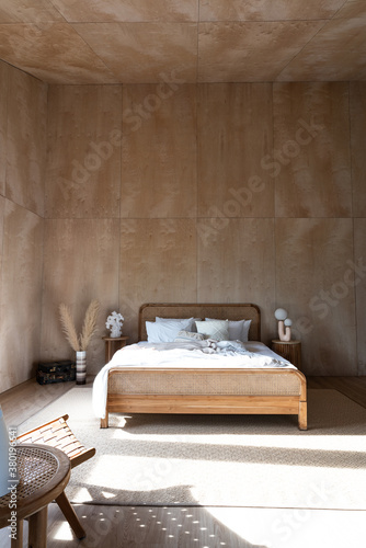 Stylish Bedroom corner with rattan headboard and bed with soft pillows setting with white pillows plywood wall on the background / cozy interior design / modern interior