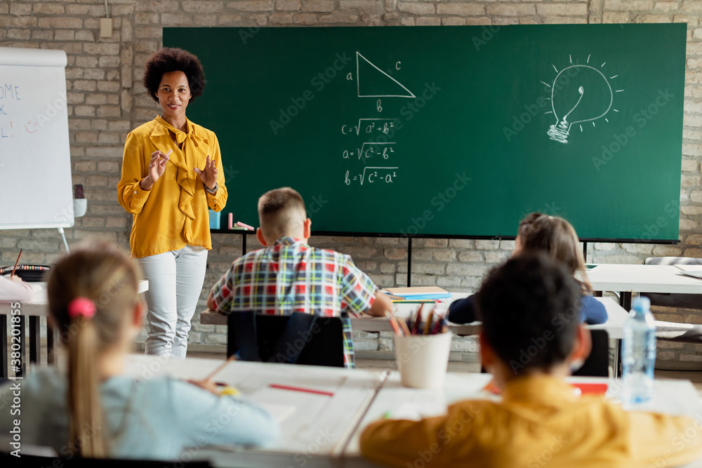 Happy black teacher talking to her students while giving math lesson in ...