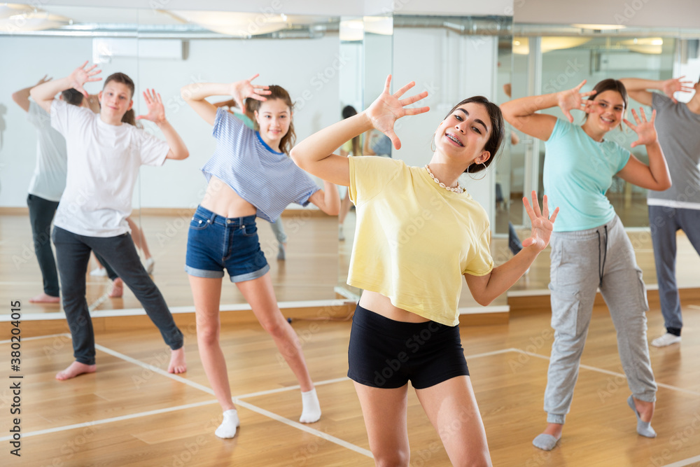 Portrait of cheerful teenage girl doing exercises during group class in dance center