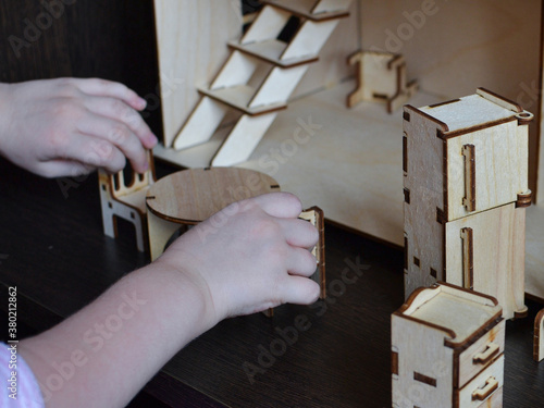 Children's hands are placing the doll's wooden furniture photo