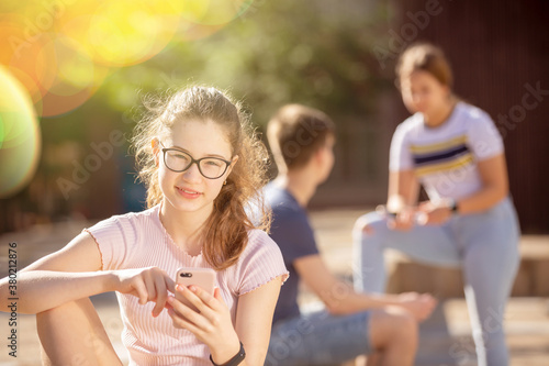 Teen girl playing on smartphone while sitting next to friends