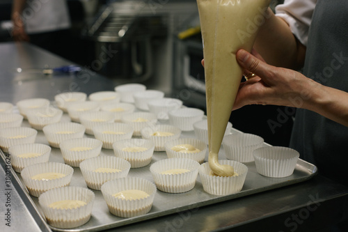 Baker filling with muffin batter a tray full of molds with a pastry bag photo