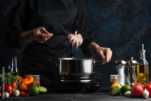 The chef in black apron cooking baby octopus on the professional kitchen. Chef's hand putting seafood into the pot with boiling water. Food concept.