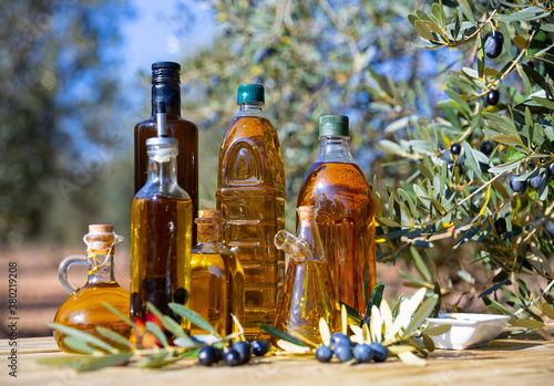 Decanters and bottles with golden olive oil, fresh and pickled olives on wooden surface outdoors