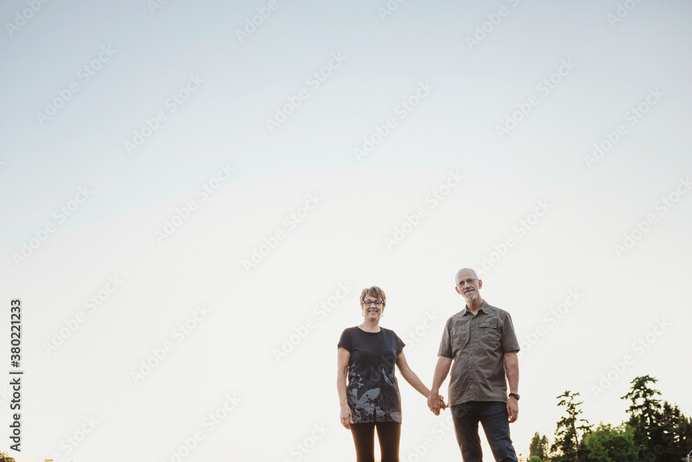 Content middle aged, retired couple holding hands together outside on lake ocean dock Content middle aged, retired couple holding hands together outside on lake ocean dock