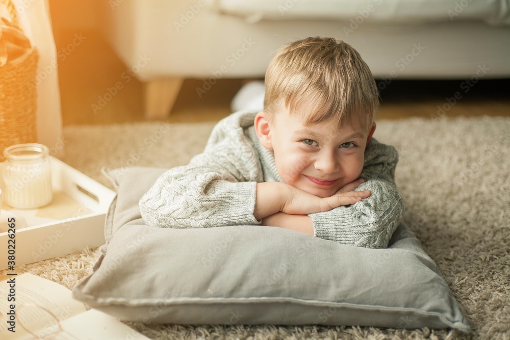 A beautiful little boy in a knitted sweater is reading by the window with a mug of hot tea. Cozy. Autumn. A beautiful little boy in a knitted sweater is reading by the window with a mug of hot tea. Cozy. Autumn.