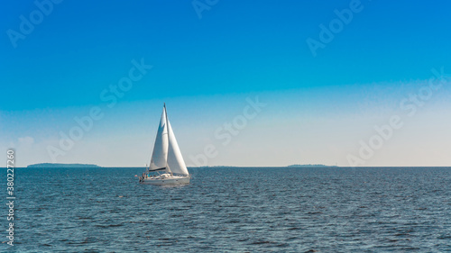 A lonely white sailing yacht sails in the open sea. Sunny day. Calm water surface