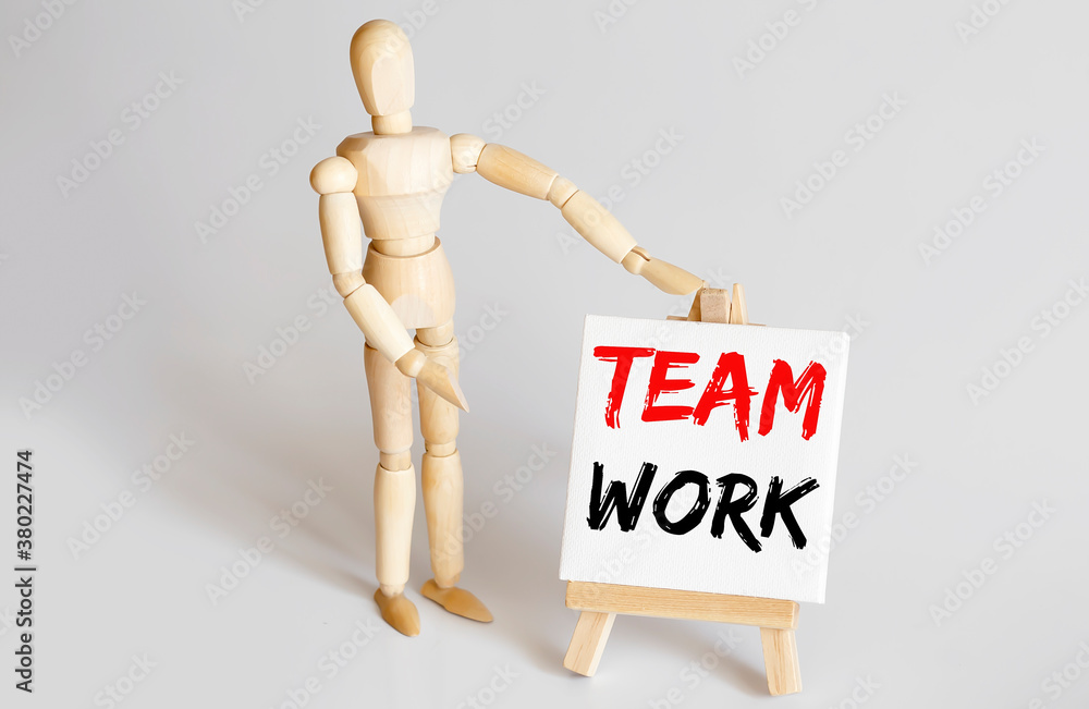 Wooden man shows with a hand to white easel with text TEAM WORK Wooden man shows with a hand to white easel with text TEAM WORK