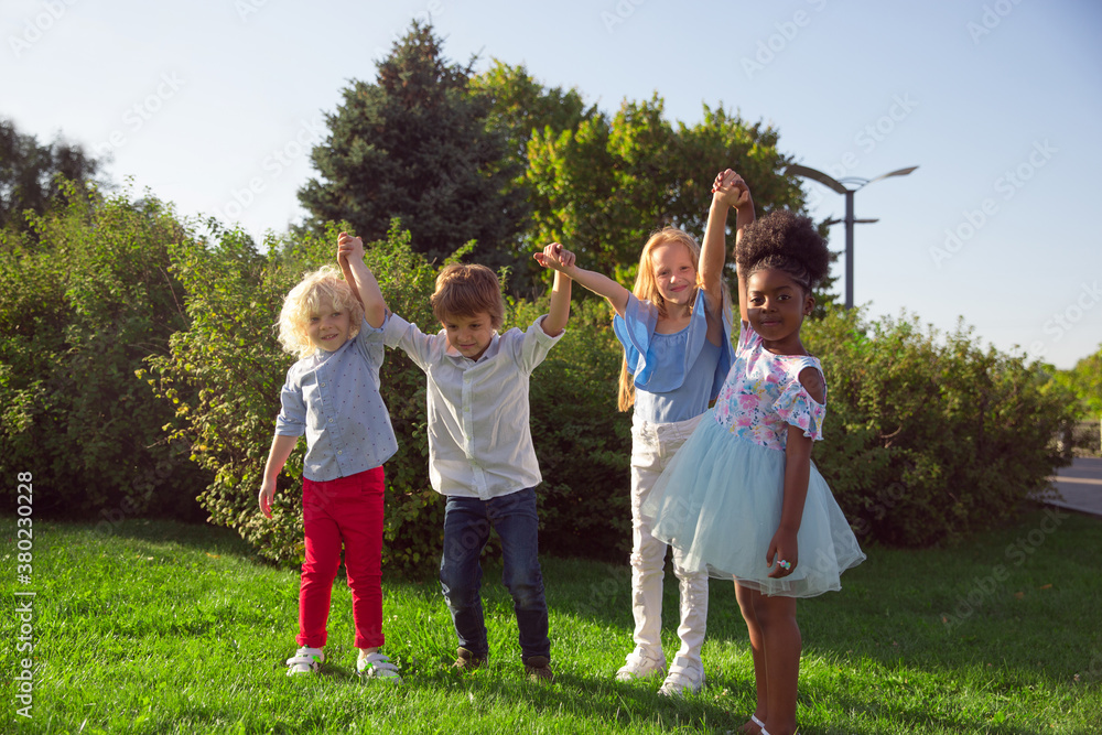 Obraz premium Moments. Interracial group of kids, girls and boys playing together at the park in summer day. Friendship has no race. Happiness, childhood, education, diversity concept. Look happy and sincere.