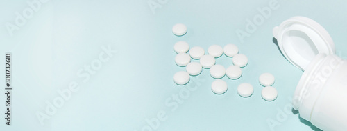 White open plastic jar with a bunch of white scattered pills on a light blue background, medicine concept, copy of the space, banner