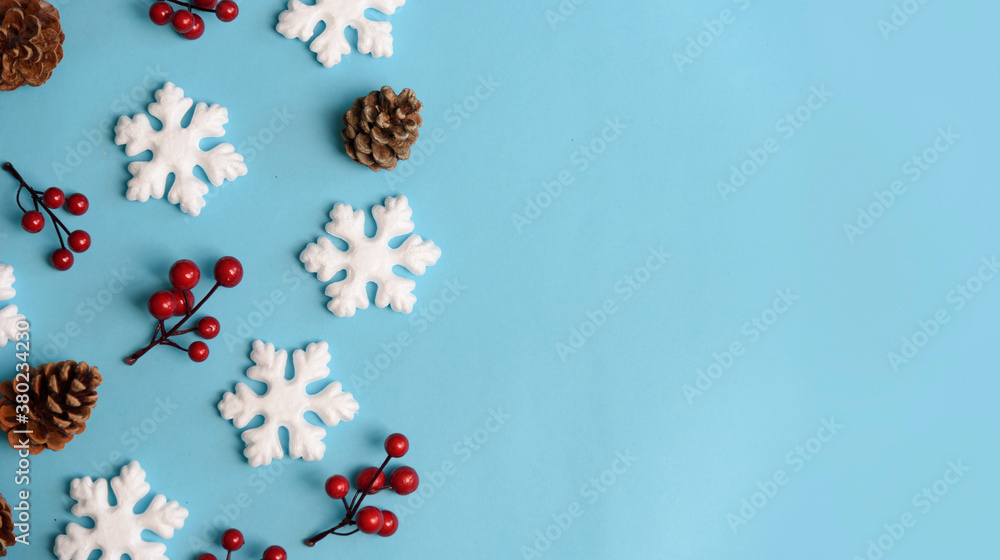 Minimal christmas, new year and winter holiday composition. Flat lay. Creative banner with snow flakes, red berry and pine cone on pastel blue background. Christmas and wintertime concept. Top view.