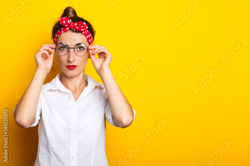 Young woman with a headband straightens her glasses on a yellow background. Banner