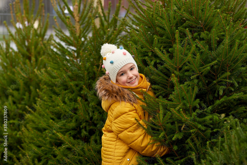 winter holidays and people concept - happy smiling little girl choosing christmas tree at street market