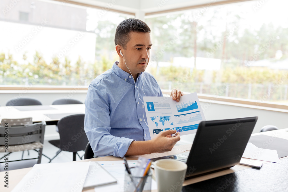 remote job, technology and people concept - middle-aged man in earphones with laptop computer and charts working at home office and having video call remote job, technology and people concept - middle-aged man in earphones with laptop computer and charts working at home office and having video call