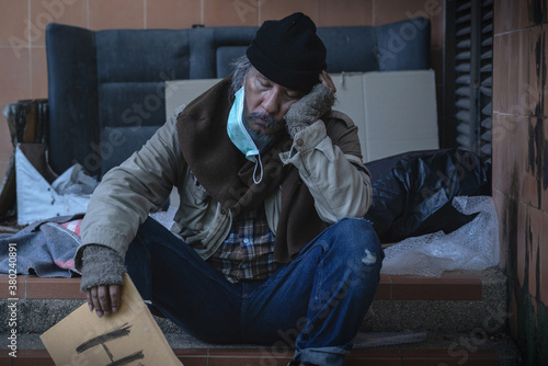 ็Homeless man, a beggar wearing a mask, sat asleep on the stairs , holding a brown cardboard with word "Help" is on the cardboard