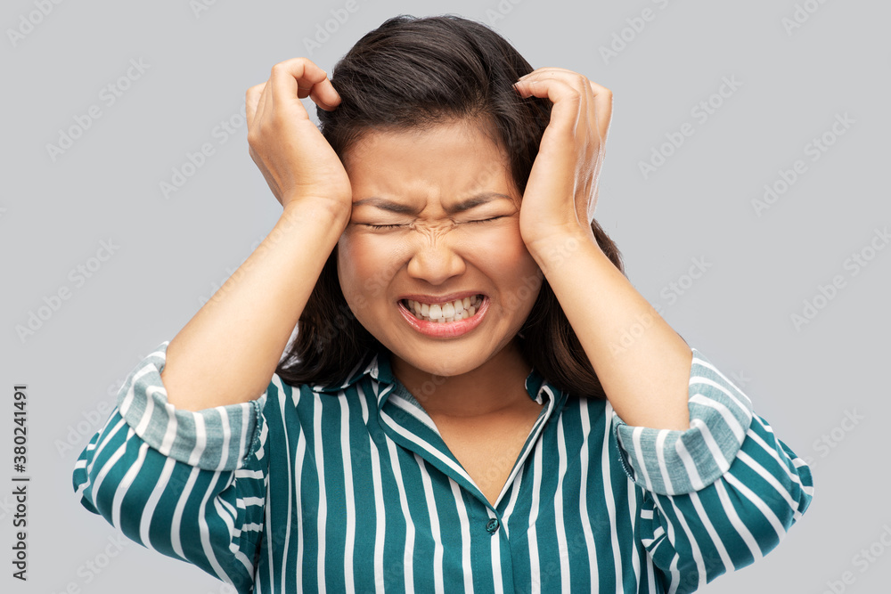 pain, stress and despair concept - stressed asian woman having headache holding to her head over grey background pain, stress and despair concept - stressed asian woman having headache holding to her head over grey background