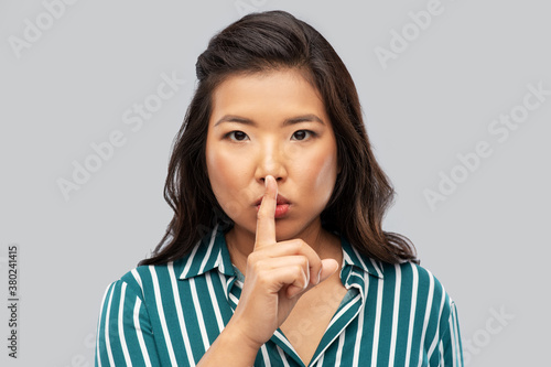 silence, confidentiality and people concept - portrait of young asian woman making hush gesture over grey background