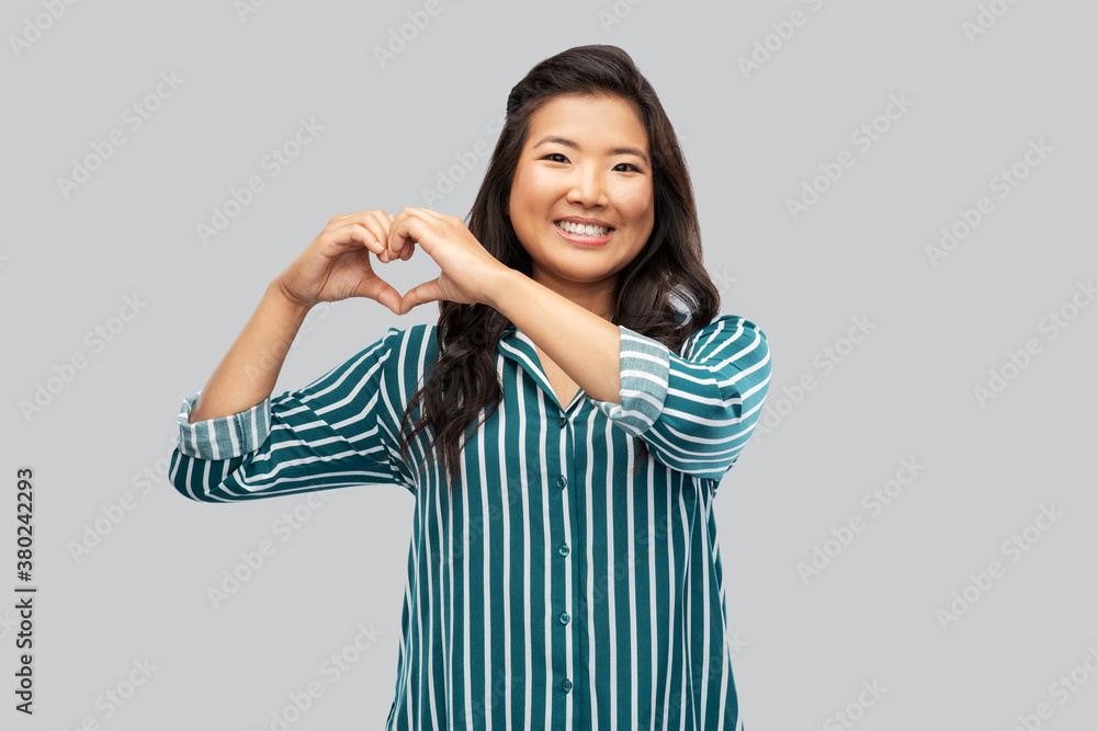 love, charity and valentines day concept - happy asian young woman showing hand heart gesture over grey background love, charity and valentines day concept - happy asian young woman showing hand heart gesture over grey background