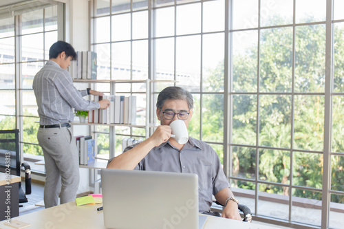 Asian middle-aged man in hand holding a coffee cup sipping on the desk in the office.