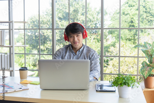 A young Asian businessman listens to music on a desk on a glass window balcony.