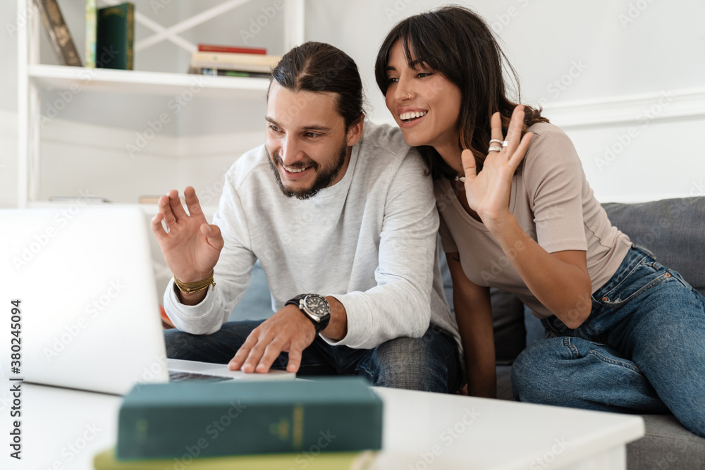 Image of cute cheerful couple using laptop and waving hands Image of cute cheerful couple using laptop and waving hands