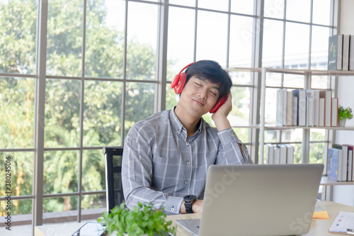 A young Asian businessman listens to music on a desk on a glass window balcony.