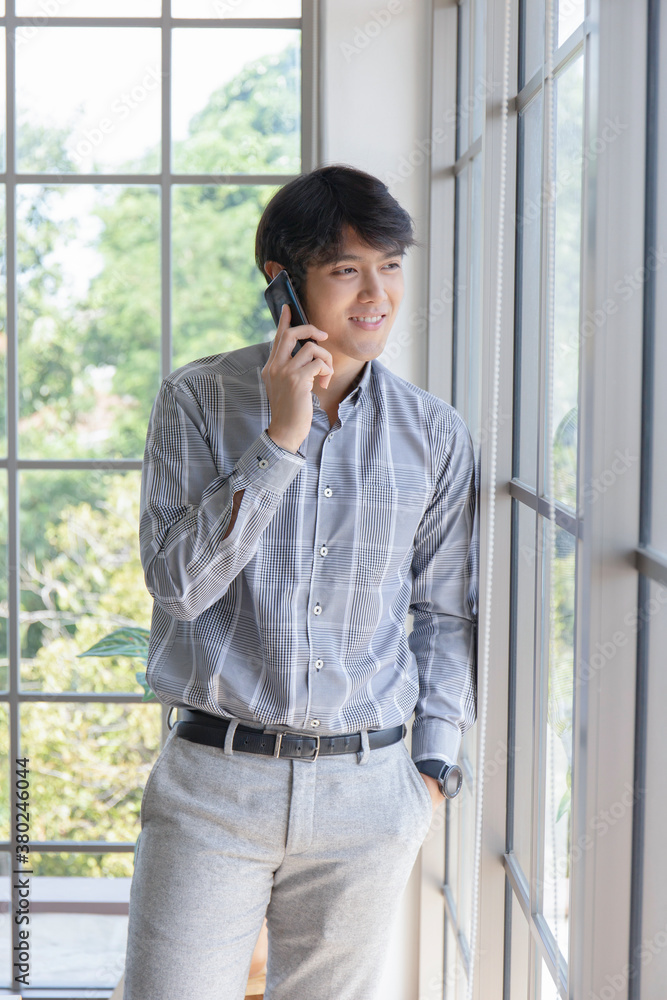 A young Asian businessman stands on the balcony of a window talking on the phone. A young Asian businessman stands on the balcony of a window talking on the phone.