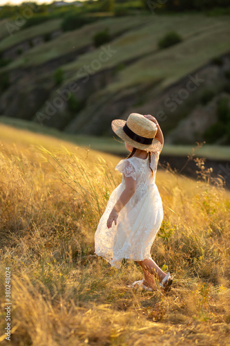 A little girl walks in the field with a hat. Beautiful girl in a white field and a hat. Girl walks in the field. Children's Day. Beautiful child. Elegant baby. Girl with pigtails
