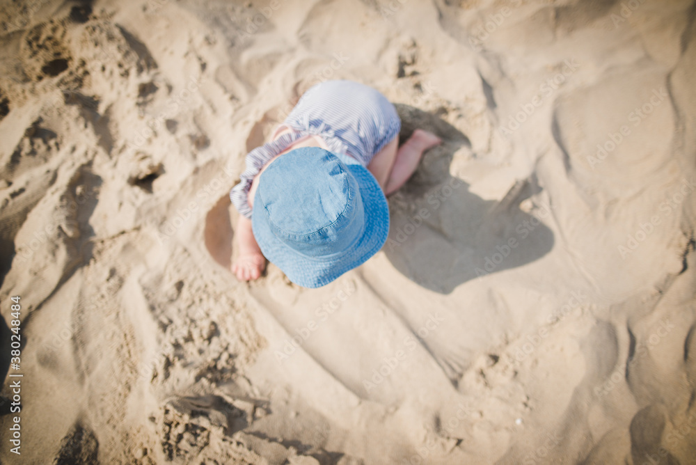 Baby girl playing on a beach in sand, wearing baby swimm suit and hat, crawling Baby girl playing on a beach in sand, wearing baby swimm suit and hat, crawling