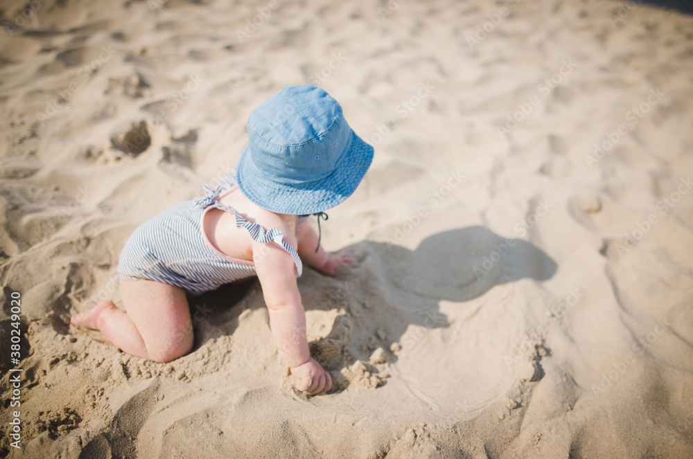Baby girl playing on a beach in sand, wearing baby swimm suit and hat, crawling Baby girl playing on a beach in sand, wearing baby swimm suit and hat, crawling