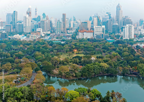 Urban skyline of Bangkok  the vibrant capital city of Thailand  with modern high rise skyscrapers in background and lush greenery by a lake in beautiful Lumphini Park in foreground on a hazy morning  