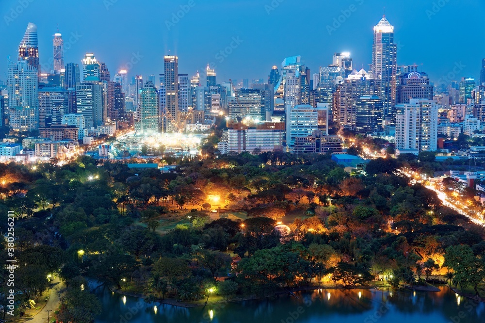 Beautiful night skyline of Bangkok, capital city of Thailand, with crowded modern high rise skyscrapers in background & lamp lights glistening in the forests of Lumphini Park under blue twilight sky