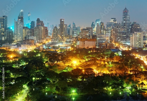 Urban skyline of Bangkok, the fast developing capital city of Thailand, with modern high-rise skyscrapers in background and street lights glistening in beautiful Lumphini Park under blue twilight sky