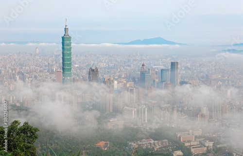 Aerial view of Downtown Taipei, capital city of Taiwan, on a foggy spring morning with Taipei 101 Tower above clouds amid skyscrapers in Xinyi Financial District & Datun Mountain in distant background