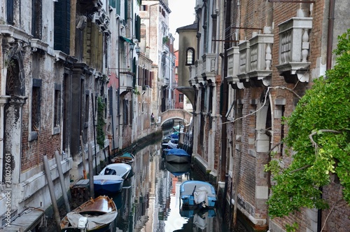 Canal in Venice, Italy, boats in the water, view towards a nostalgic stone bridge with cracked paint, reflections in water, historic buildings 