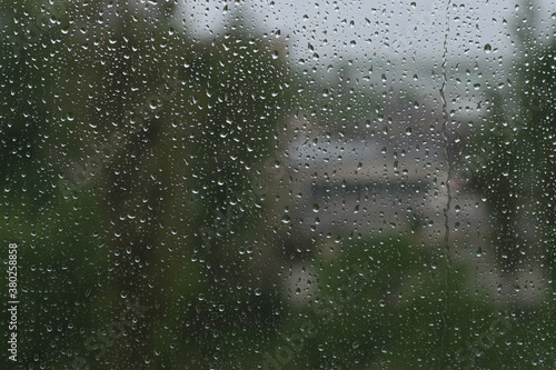 Raindrops on the glass, against the background of blurred green trees and buildings